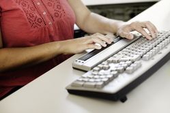 Nahaufnahme einer am Tisch sitzenden Frau, die einen Braille-Zeilenleser bedient.