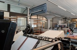 Foto der Druckerei-Halle. Im Vordergrund erkennt man eine Druckmaschine, die auf grosse Bogen Papier Braille druckt.